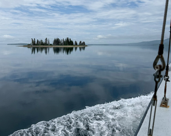 Glassy water of the Bras d’Or Lake in Cape Breton with a small island with tree in the background.