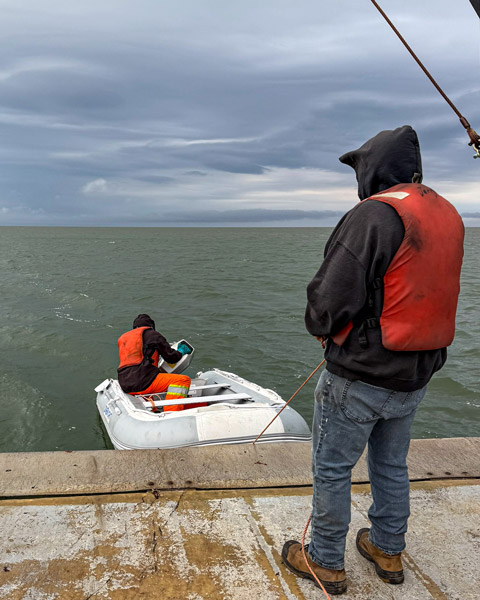 Small inflatable boat in the water off that back of a larger ship.